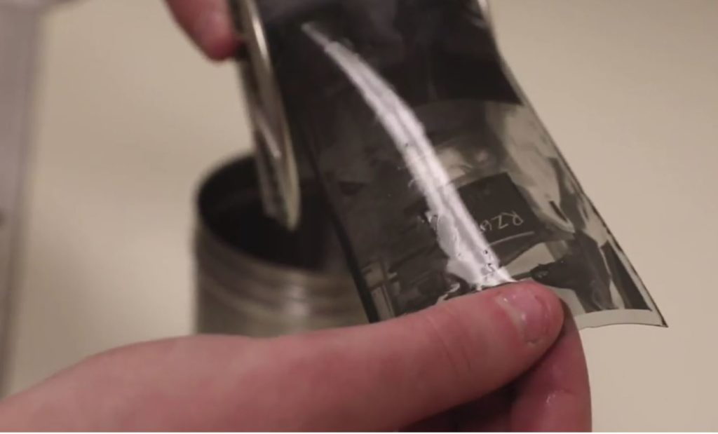 A hand is shown holding a piece of black and white film from a camera -- close up on the hand and strip of flim.