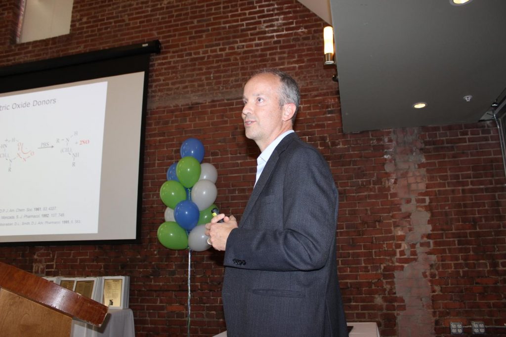 Mark Schoenfisch UNC's Inventor of the Year speaks at awards celebration with podium and balloons in background.