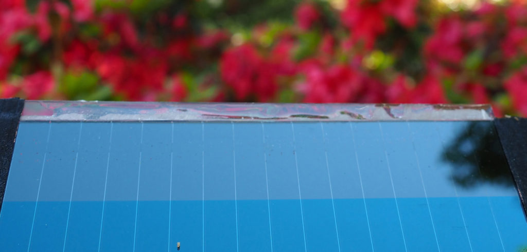 Pictured is a perovskite solar mini-module. Pictured is a perovskite solar mini-module in front of the Old Well on campus .... trees are reflected in the solar panel's mirror-like surface.