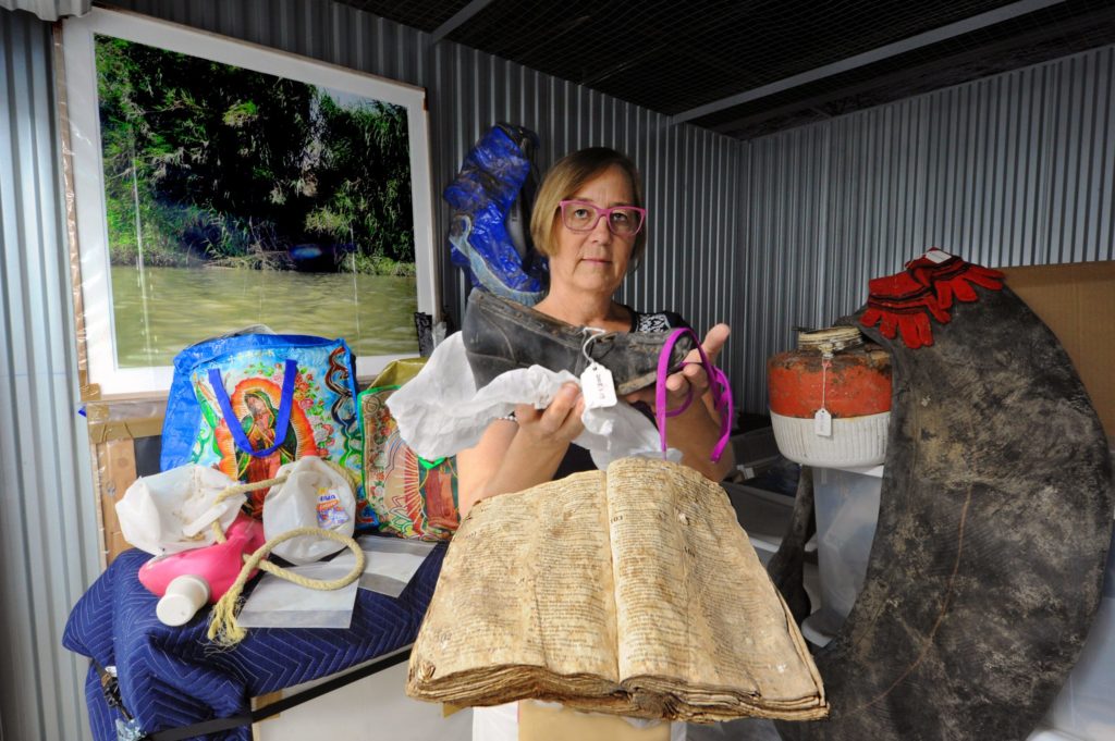 Susan Harbage Page holds a number of the objects she has collected at the U.S. Mexico border like a Bible, a shoe, an inner tube/raft, and more. (photo by Donn Young)