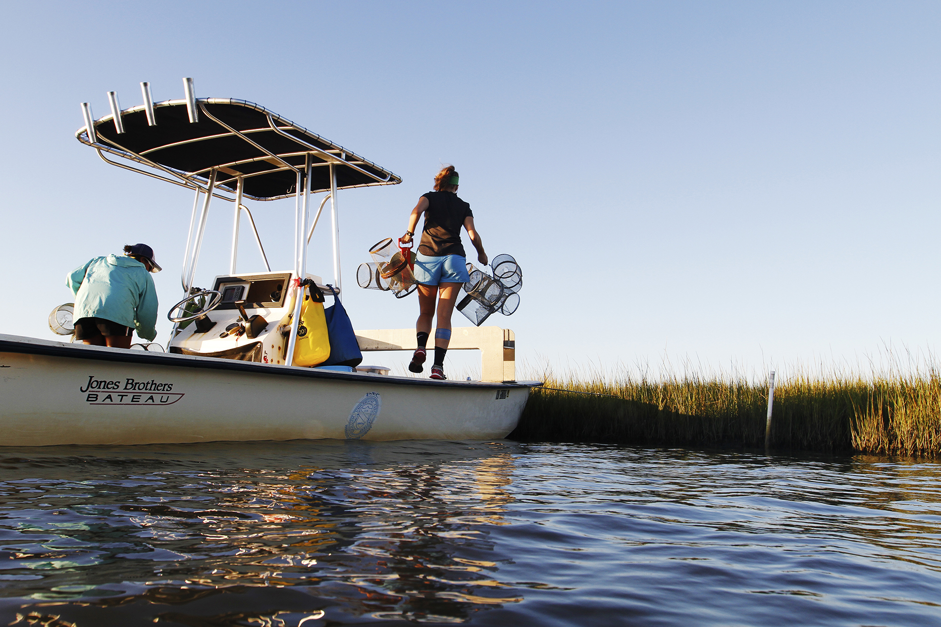 As the boat is docked near some marsh grass, Lauren Clance prepares to set out the minnow traps at the first site.