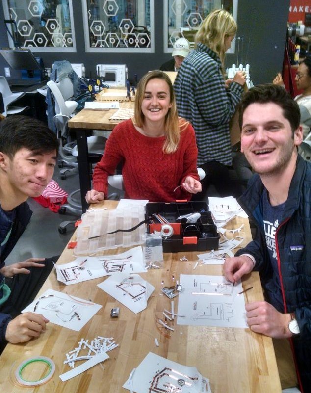 A group of APPL 110 students work on a class assignment in the BeAM makerspace at Murray Hall. Three students are sitting at a table in the makerspace, surrounded by paper and other materials used to help them brainstorm.