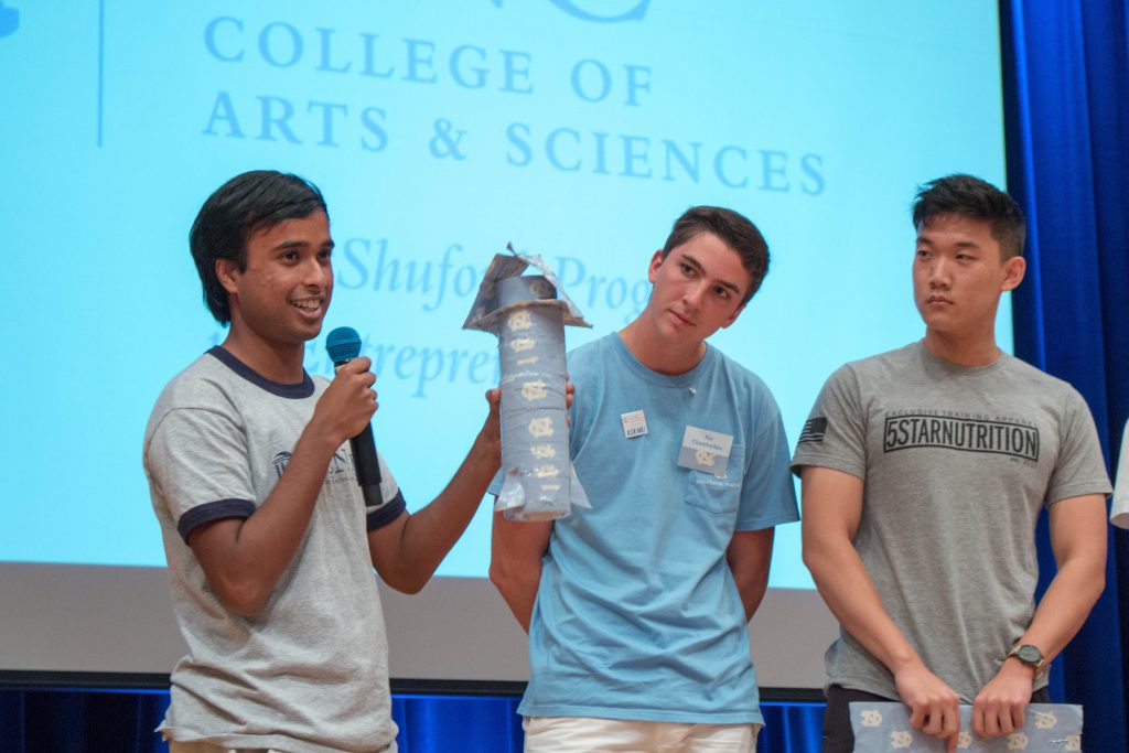A student holds up his creation: a privacy tower made from rolls of Duck Tape and cardboard, as fellow contestants look on.