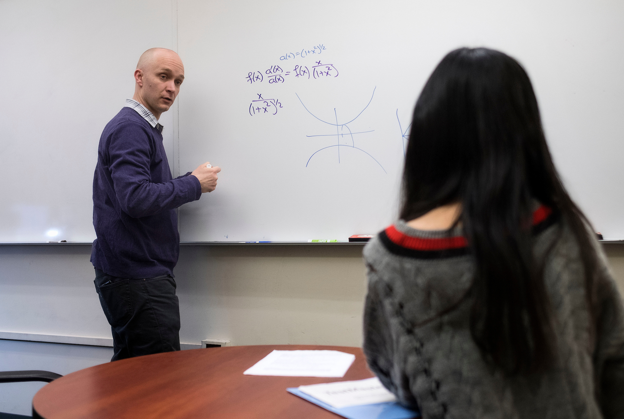 Jason Metcalfe meets with a student during office hours in Phillips Hall. ( photo by Jon Gardiner) He is drawing mathematics equations on a whiteboard while talking to the student.