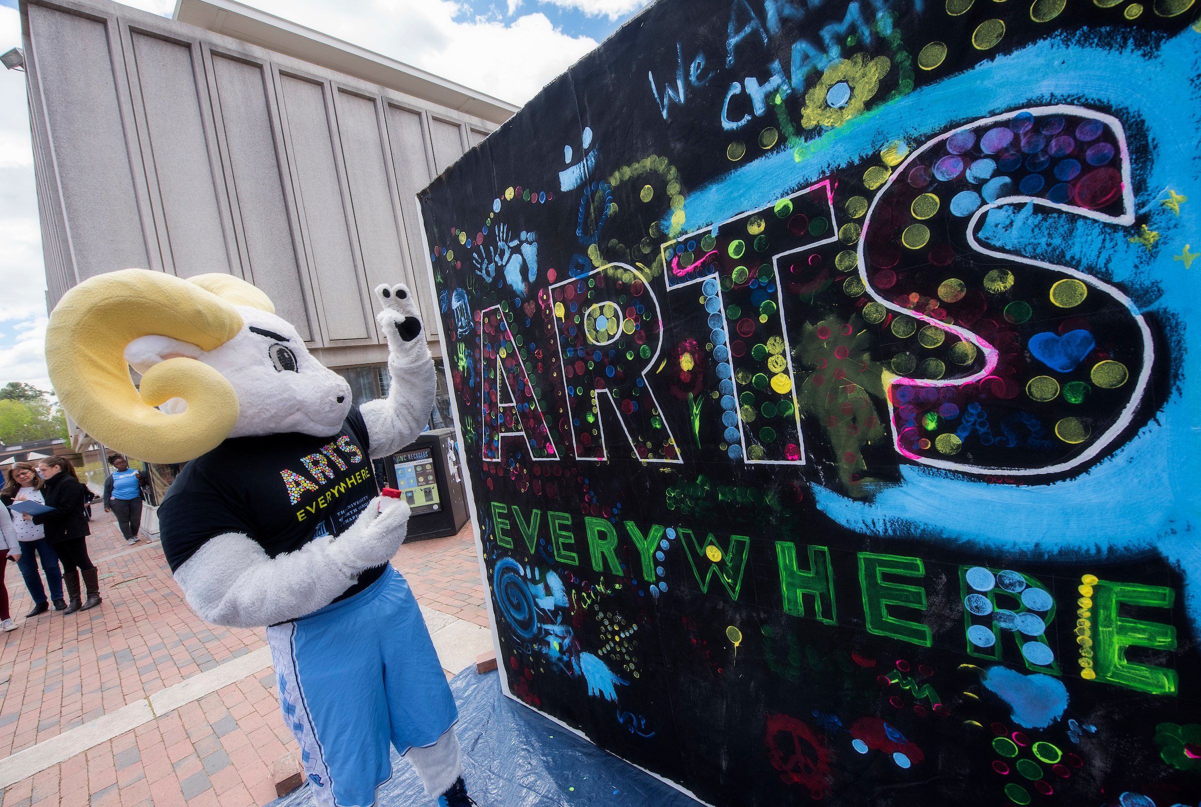 Photo of chalkboard that has "Arts Everywhere" in colorful letters with UNC's Ramses standing beside it. (photo by Jon Gardiner)