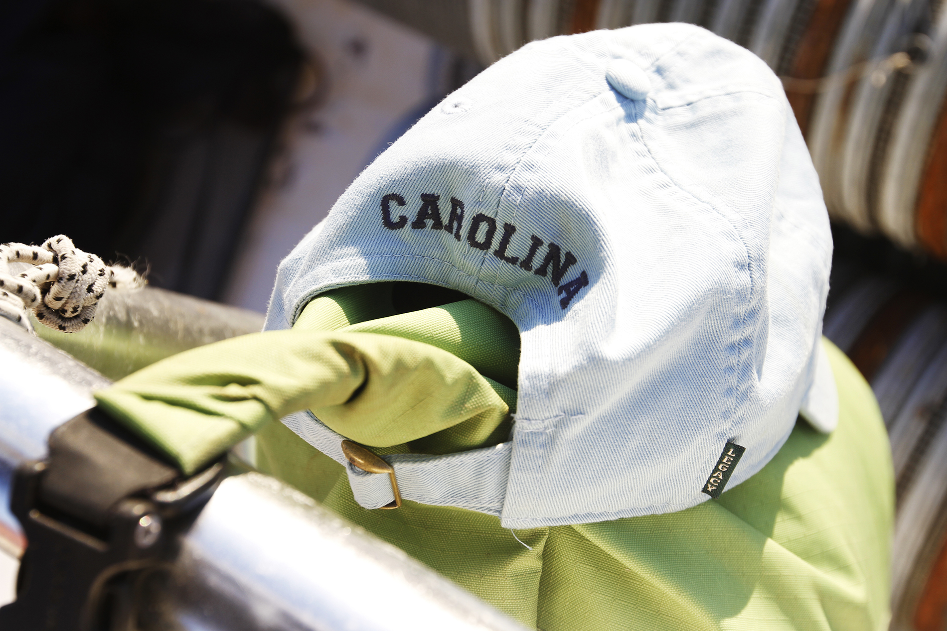 A Carolina baseball cap is shown with a bright green handle of a bookbag hooked through it. 