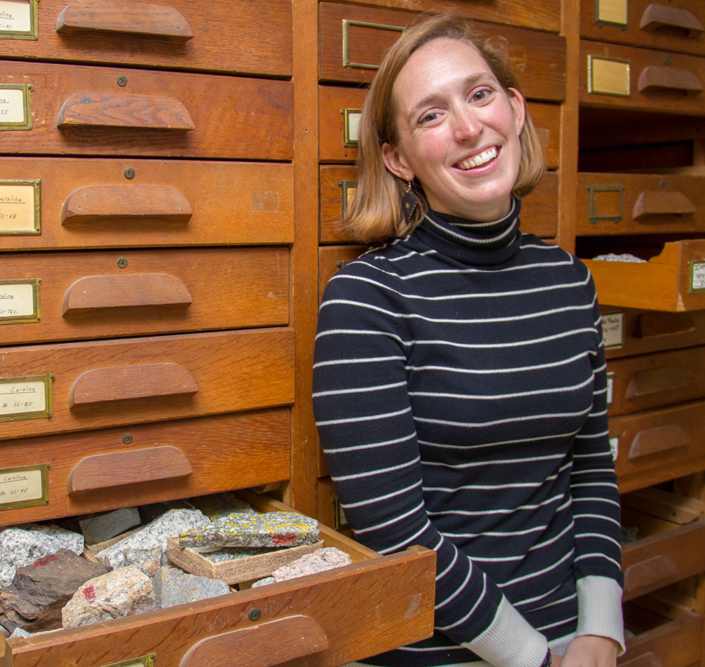 Madelyn Percy sits in front of a stack of drawers with one pulled out showing rocks. (She is a geologist)