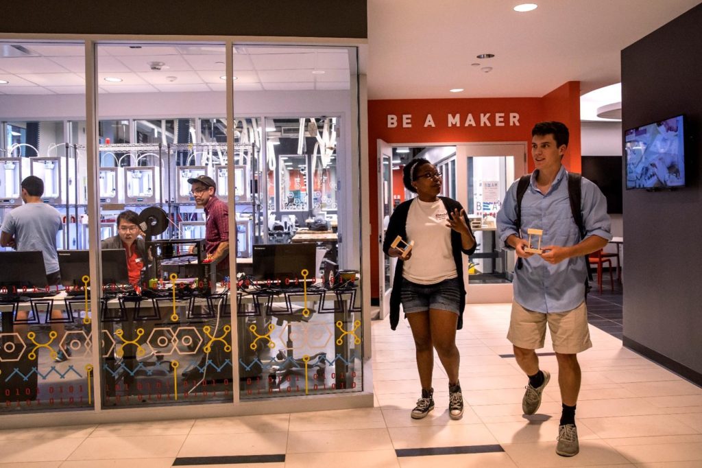 The entrance of the BeAM makerspace in Murray Hall, where students in the the new APPL 110 work to develop prototypes. (The words "Be A Maker" are emblazoned on an orange wall as two students walk by the entrance.