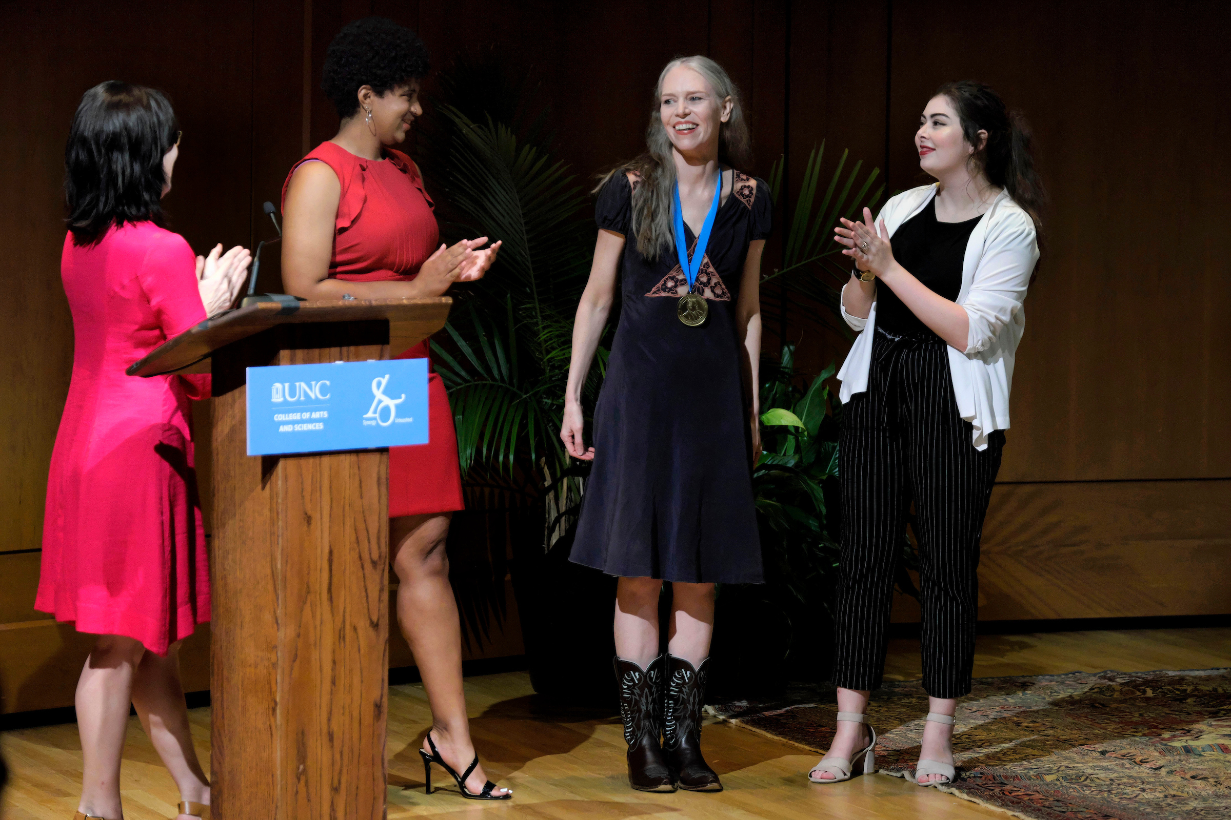 Grace Morse, left, and Savannah Bradley, Thomas Wolfe Scholars in the class of 2022, stood on either side of Gillian Welch and slipped the Wolfe medal over her head. (photo by Jon Gardiner)
