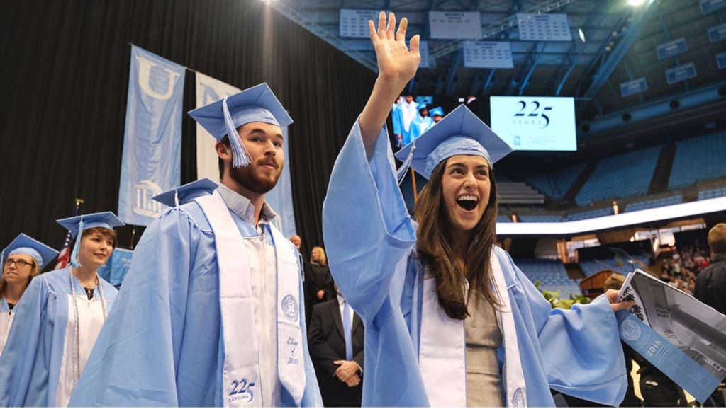 Commencement speaker Winston Crisp told students: “Find your passion — the thing that makes you want to get up every morning and step outside to meet the day." (photo courtesy of UNC-Chapel Hill). Photo shows two students in graduation robes with one student waving her hand hello at the camera.