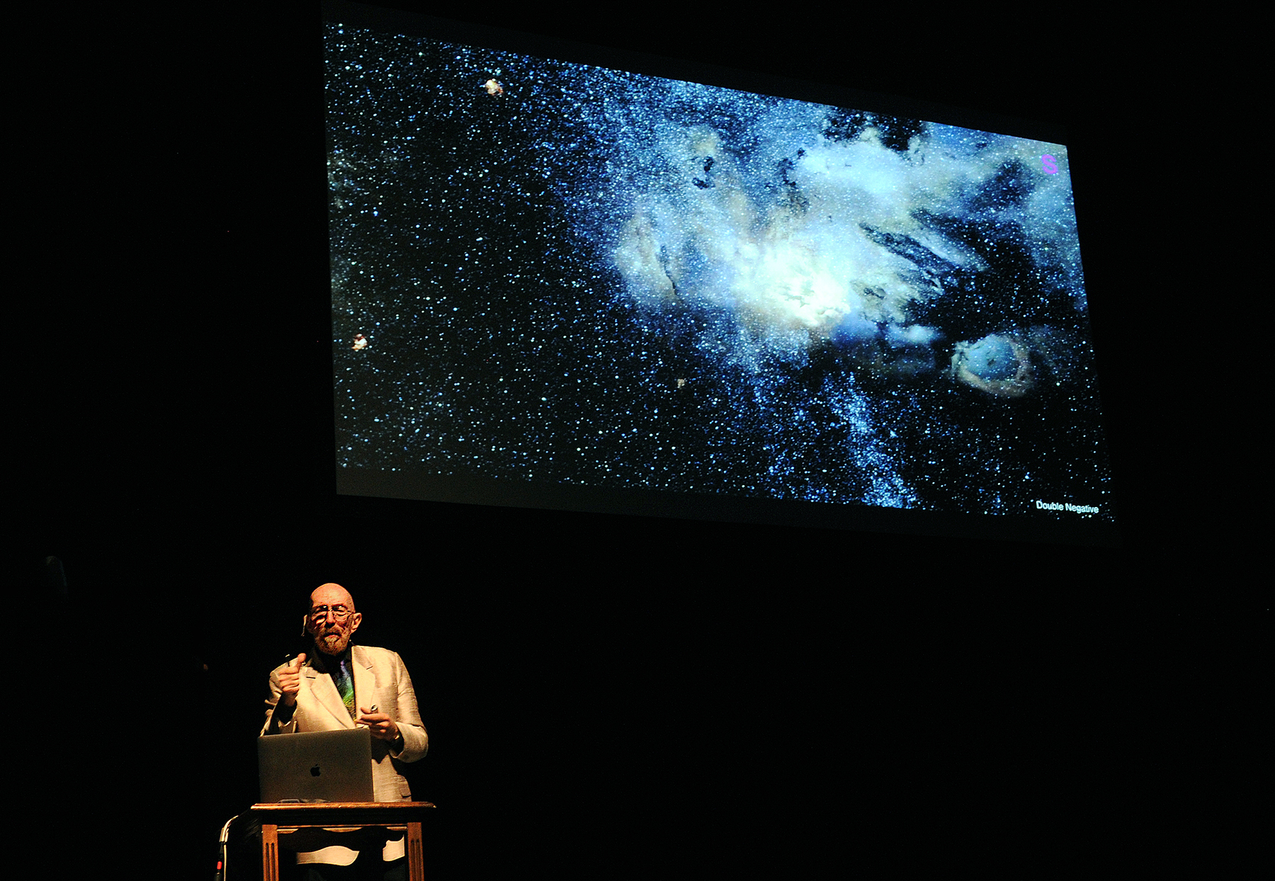 Frey lecturer Kip Thorne discussed his romance with the "warped side of the universe." (photo by Donn Young) In this photo Thorne stands in front o the audience with a big screen in the background with a picture of some of these phenomena like black holes, worm holes, etc.