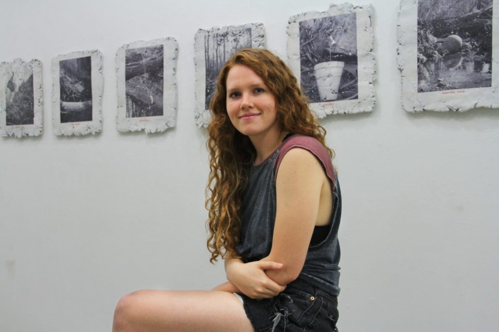 Student Meredith Emery sits in front of her artwork on the walls.