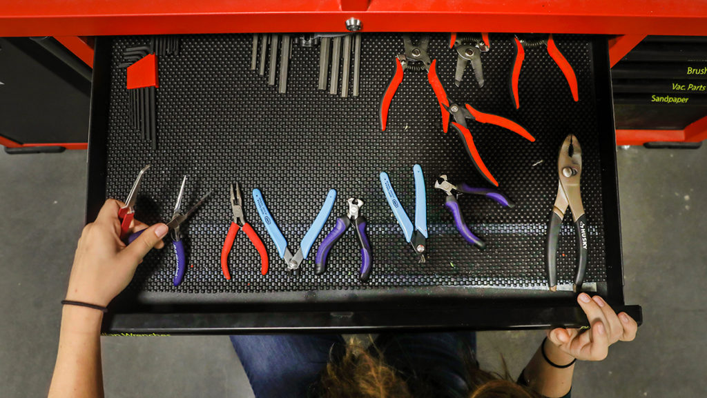 Photo shows a closeup of a large board holding a variety of tools and a closeup of hands picking up the tools.