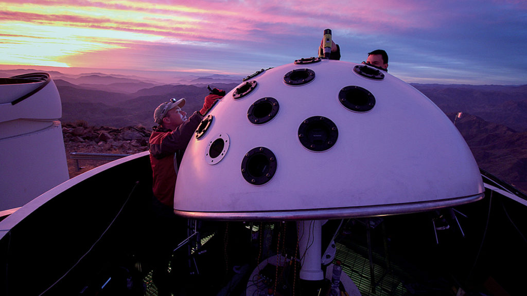 A photo of a man working on the everyscope which looks like a giant mushroom with a purple twighlight sky in the background.