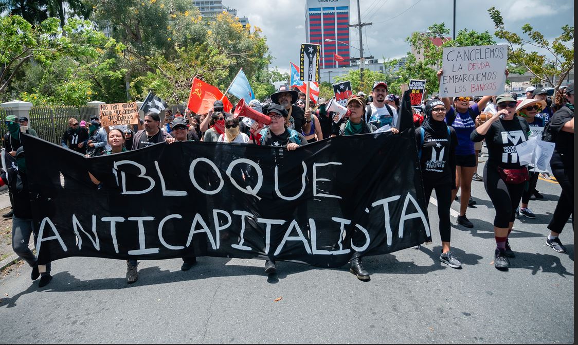 A 2019 May day sign reads: "Let's cancel the debt. Let's seize the banks."