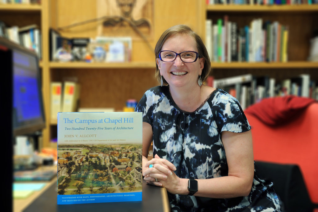 JJ Bauer, teaching assistant professor in the department of art and art history, helps illuminates the stories behind Carolina's buildings in a book on campus architecture. (photo by Donn Young). In the picture she is in her office holding a copy of the book and facing the camera.