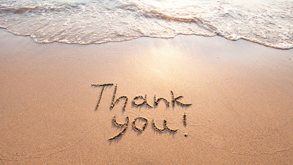 The words "Thank You!" are written on the sand of a beach.